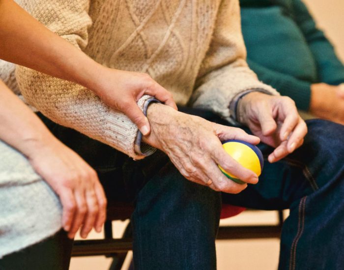 An elderly person receives support from a caregiver, holding hands indoors, showcasing compassion.